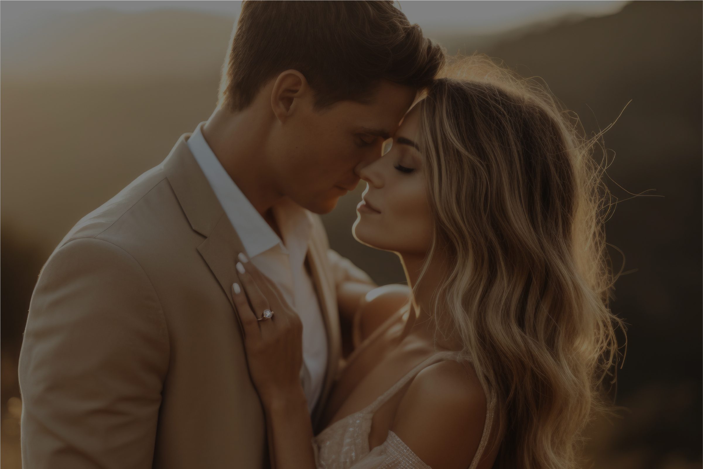 Close-up of a newlywed couple sharing an intimate moment at sunset, with their foreheads gently touching and the bride's hand resting on the groom's lapel, showcasing her engagement ring.